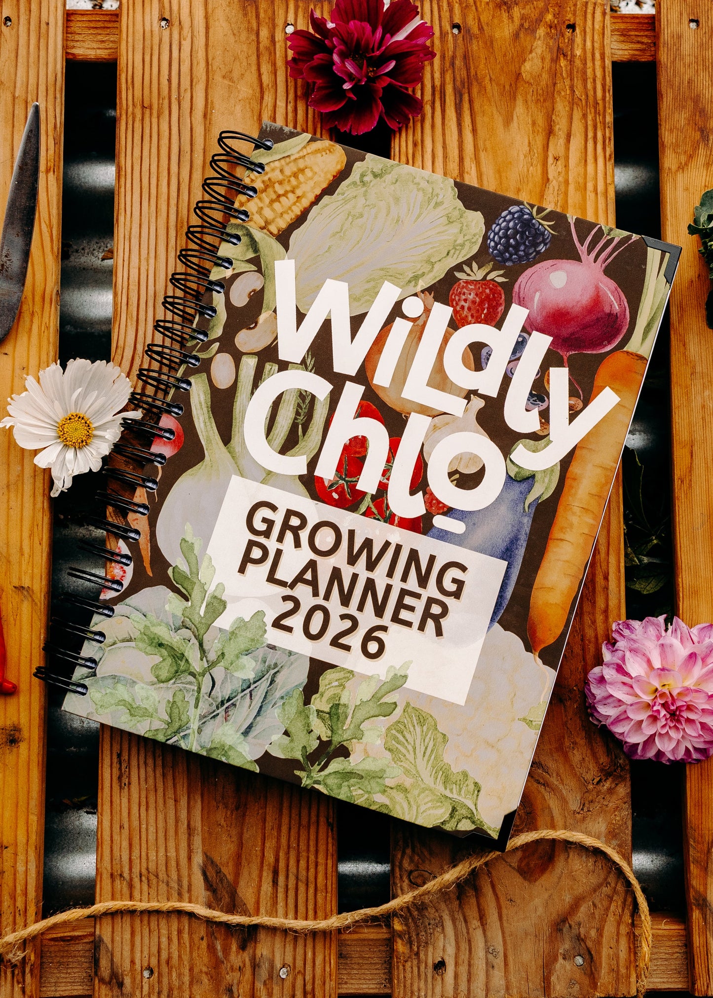 Gardening planner titled 'Wildly Chlo' on a wooden surface with gardening tools and vegetables.